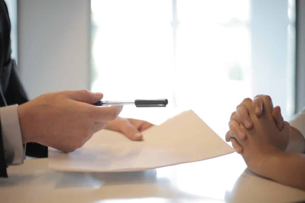 A person handing a pen and paper to another in an interview skill test